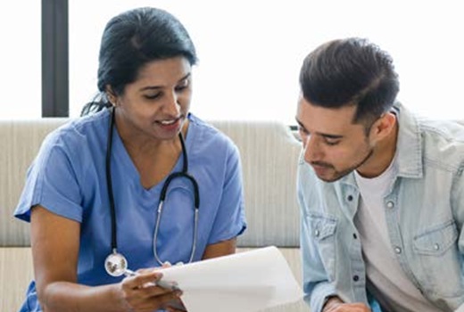 A clinician in scrubs with a stethoscope around her neck reviews paperwork with a patient.