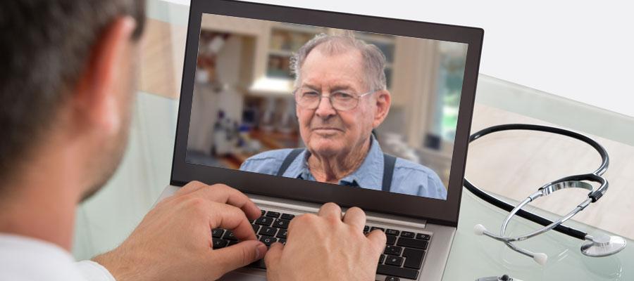 A physician talks with a rural patient appearing on a laptop computer screen via a telehealth app.